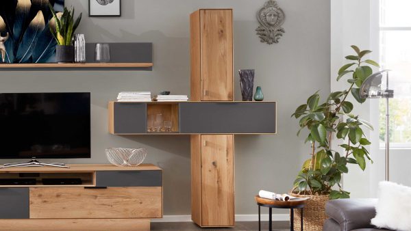 Das Interliving Wohnzimmer Serie 2005 - Hängeschrank-Set 117 951 zeigt Holz- und graue Schränke, einen Fernseher, Glasdekor, eine große Pflanze, Wandvasen und moderne Kunst an einer hellgrauen Wand mit einem dekorativen Gesichtsmotiv.