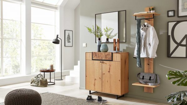 Das Interliving Garderoben Serie 6006 - Komplett-Set 62 1001 zeigt einen modernen Eingangsbereich mit großen Fenstern, Holzmöbeln, Spiegel und Garderobe. Schuhe, Taschen und Jacken sind ordentlich angeordnet, während Pflanzen und Kunstwerke bei natürlichem Licht dekorative Akzente setzen.