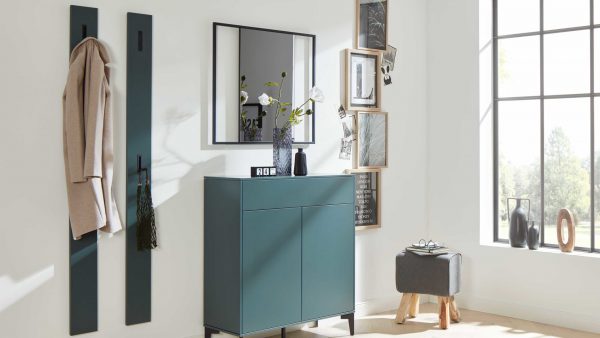 Moderner Eingangsbereich mit der Interliving Garderoben Serie 6009 - Wandgarderobe 661911, einem tealfarbenen Aufbewahrungsschrank, wandmontierten Garderobenständern mit beigem Mantel und Tasche, dekorativem Spiegel, gerahmter Kunst, grauem Hocker und einem großen Fenster für natürliches Licht.