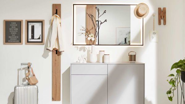 Moderner Eingangsbereich mit der Interliving Garderoben Serie 6009 - Wandgarderobe 661911, gepaart mit einem weißen Schrank, dekorativen Vasen, einem großen hinterleuchteten Spiegel, Wandhaken mit Hut und Mantel, gerahmter Kunst, Koffer, Tasche und einer grünen Pflanze in der Ecke.