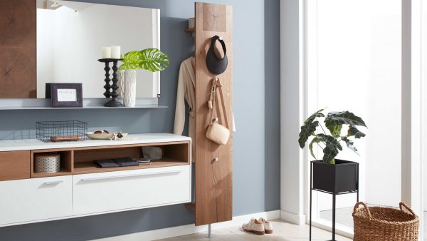 In einem modernen Eingangsbereich hält die Interliving Garderoben Serie 6010 Wandgarderobe 511919 einen hellbraunen Mantel, einen Hut und eine Tasche. Eine schwebende Konsole, ein Spiegel, Kerzen, eine Pflanze, Schuhe und ein Korb vervollständigen das helle, minimalistische Dekor.