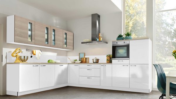 Moderne Küche mit glänzend weißen Schränken, Oberschränken aus hellem Holz, eingebautem Backofen, Dunstabzugshaube aus rostfreiem Stahl und großen Fenstern, die Tageslicht hereinlassen. Auf der Arbeitsplatte stehen Kochutensilien, ein Mixer und frische Produkte.