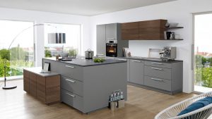 Moderne Küche mit grauen und hölzernen Schränken, einer Insel mit Schubladen, eingebautem Ofen, Kaffeemaschine und großen Fenstern mit Blick ins Grüne. Helle Holzböden und moderne Möbel vervollständigen den Raum.