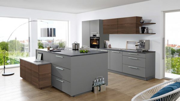 Moderne Küche mit grauen und hölzernen Schränken, einer Insel mit Schubladen, eingebautem Ofen, Kaffeemaschine und großen Fenstern mit Blick ins Grüne. Helle Holzböden und moderne Möbel vervollständigen den Raum.