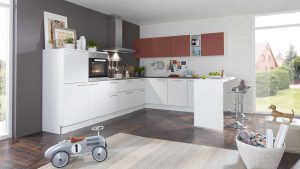 Moderne Küche mit weißen und braunen Schränken, Geräten aus Edelstahl und einer Frühstücksbar mit Hockern. Große Fenster lassen viel natürliches Licht herein. Ein Spielzeugauto, ein Korb mit Spielzeug und ein Hund stehen im Vordergrund auf einem Teppich.