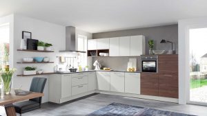 Moderne Küche mit weißen und hölzernen Schränken, eingebautem Ofen, offenen Regalen mit Geschirr und Pflanzen, einer Spüle unter einem Fenster und einem Esstisch mit Stühlen und einer Vase mit Tulpen. Durch die vielen Fenster fällt viel Licht ein.
