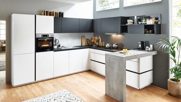 Moderne Küche mit weißen und schwarzen Schränken, Einbaubackofen, Arbeitsplatten, einer kleinen Bar mit zwei Zitronen, Holzfußboden, Zimmerpflanzen, Regalen mit Geschirr und großen Fenstern, die natürliches Licht hereinlassen.