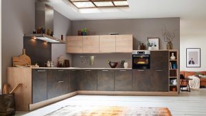 Moderne L-förmige Küche mit Holz und dunklen Schränken, eingebautem Ofen und einem Oberlicht. Offene Regale zeigen Dekoration und Küchenutensilien. Der angrenzende Wohnbereich mit einem Sofa und gerahmten Kunstwerken ist teilweise sichtbar.