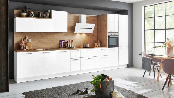 Moderne Küche mit glänzend weißen Schränken, Aufkantung aus Holz und Einbaugeräten. Ein Esstisch mit Stühlen steht neben einem großen Fenster, das natürliches Licht hereinlässt. Ein grauer Teppich und Pflanzendekor vervollständigen den gemütlichen, stilvollen Raum.