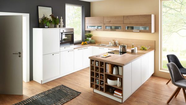 Moderne Küche mit weißen und hölzernen Schränken, eingebautem Ofen, Kochfeld, großem Fenster, offenen Regalen mit Küchenutensilien, Topfpflanzen und einem Esstisch aus Holz mit grauen Stühlen auf einem Holzboden.