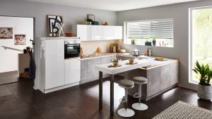 Moderne Küche mit weißen und grauen Schränken, Einbaubackofen, Bartheke mit zwei Hockern, großem Fenster mit Jalousien, Pflanzen und verschiedenen Küchenutensilien, die ordentlich auf Theken und Regalen angeordnet sind.