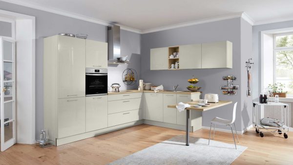 Moderne Küche mit beigen Schränken, Einbaubackofen, Hängeschränken und einem kleinen Tisch mit zwei Hockern. Der helle Holzboden, die grauen Wände und die großen Fenster sorgen für eine helle, luftige Atmosphäre. Küchenutensilien und Kleingeräte sind sichtbar.