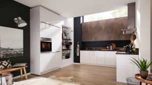 Moderne Küche mit glänzend weißen Schränken, eingebautem Ofen, Holzakzenten, offenen Regalen mit Dekoration, Kaffeemaschine und Topfpflanzen. Ein großes Fenster lässt natürliches Licht herein und unterstreicht das klare, minimalistische Design.