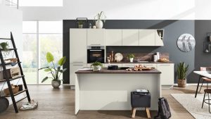 Moderne Küche mit cremefarbenen Schränken, einer hölzernen Arbeitsinsel, einem eingebauten Ofen, Pflanzen, einem Leiterregal, Wandkunst und großen Fenstern, die viel Tageslicht hereinlassen. Kochzutaten und Utensilien befinden sich auf der Theke.