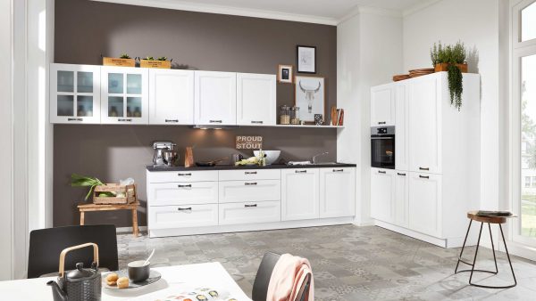Moderne Küche mit weißen Schränken, schwarzer Arbeitsplatte und Geräten. Pflanzen, hölzerne Akzente und dekorative Gegenstände sorgen für Wärme. Das Sonnenlicht strömt durch große Fenster und erhellt den Raum.