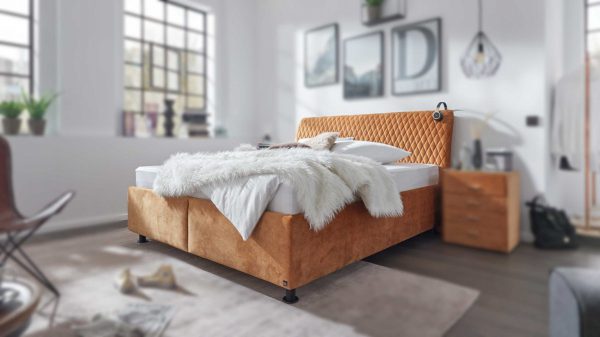 Ein stilvolles Schlafzimmer mit der Interliving Polsterbett Serie 1411 - Polsterbett VZ2, weißer Bettwäsche und einer flauschigen Decke. Das Sonnenlicht fällt durch zwei große Fenster ein und bringt die moderne Einrichtung und die Holzmöbel zur Geltung.