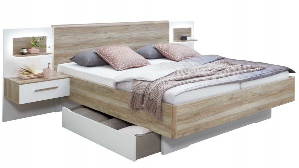 Die rauch ORANGE Bettanlage Helene mit Hängekonsolen ist ein modernes Holzbett mit Kopfteil, zwei hängenden Beistelltischen, Regalen, zwei Kissen, einer Decke und einer offenen Schublade darunter für Bettwäsche.