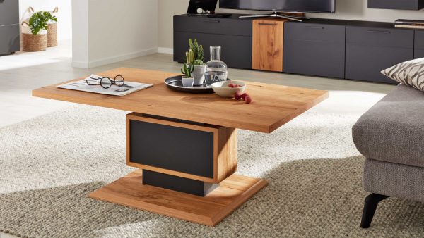 Der Interliving Wohnzimmer Serie 2023 - Couchtisch CTKL120 mit schwarzem Sockel steht auf einem hellen Strukturteppich und hält ein Tablett mit Kakteen, einer Glasflasche, einer Obstschale und einer Brille auf einer gefalteten Zeitung.